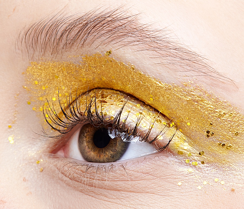 Closeup macro shot of  human female eye. Woman with unusual glitter glitzy vogue face beauty makeup. Girl with perfect skin and yellow smoky eyes eye shadows