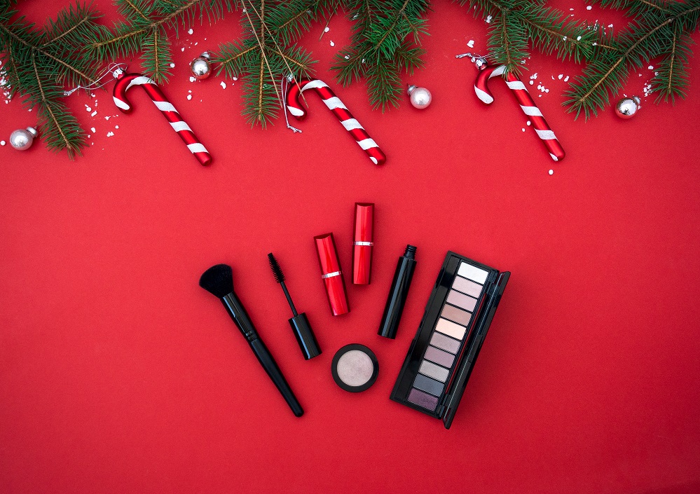 Flat lay composition with makeup cosmetic products and Christmas decor on red background. Top view. Beauty banner for sale.