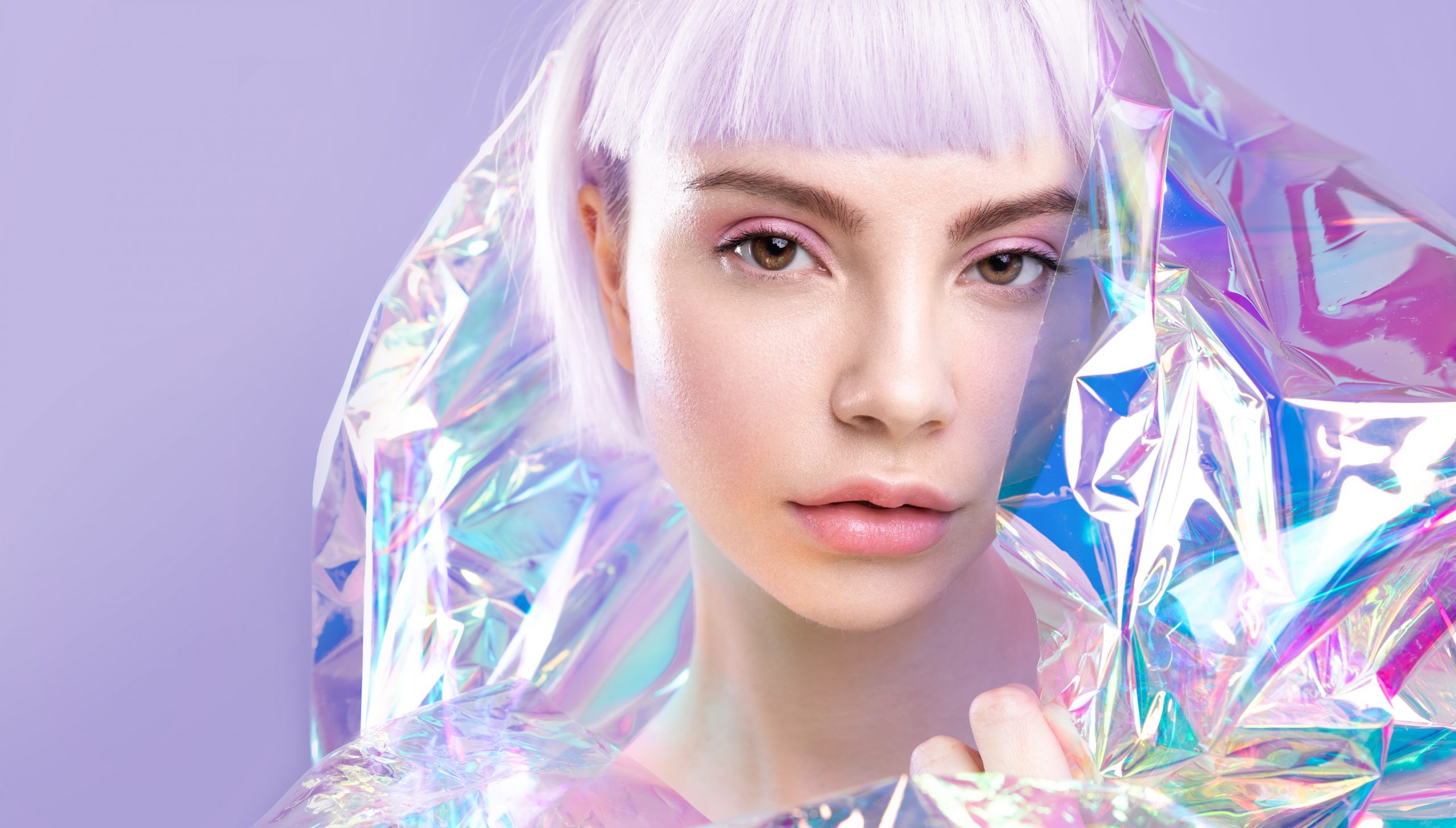 Cool sensual young blond girl with ideal brows, purple hair and perfect makeup, healthy glowing skin in colourful iridescent foil Cool modern young girl with ideal brows, purple hair and perfect makeup, healthy glowing skin, blond short hairs in colourful iridescent foil. Creative portrait of blonde, ad of cosmetics and make up products.