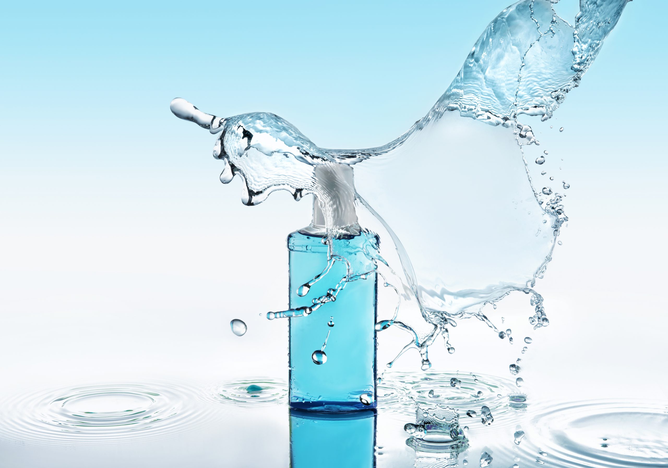 Moisturizing shampoo on the blue water background with big splash Blue moisturizing shampoo stays on the blue water background with big splash above the bottle and with many water drops and water waves around the bottle