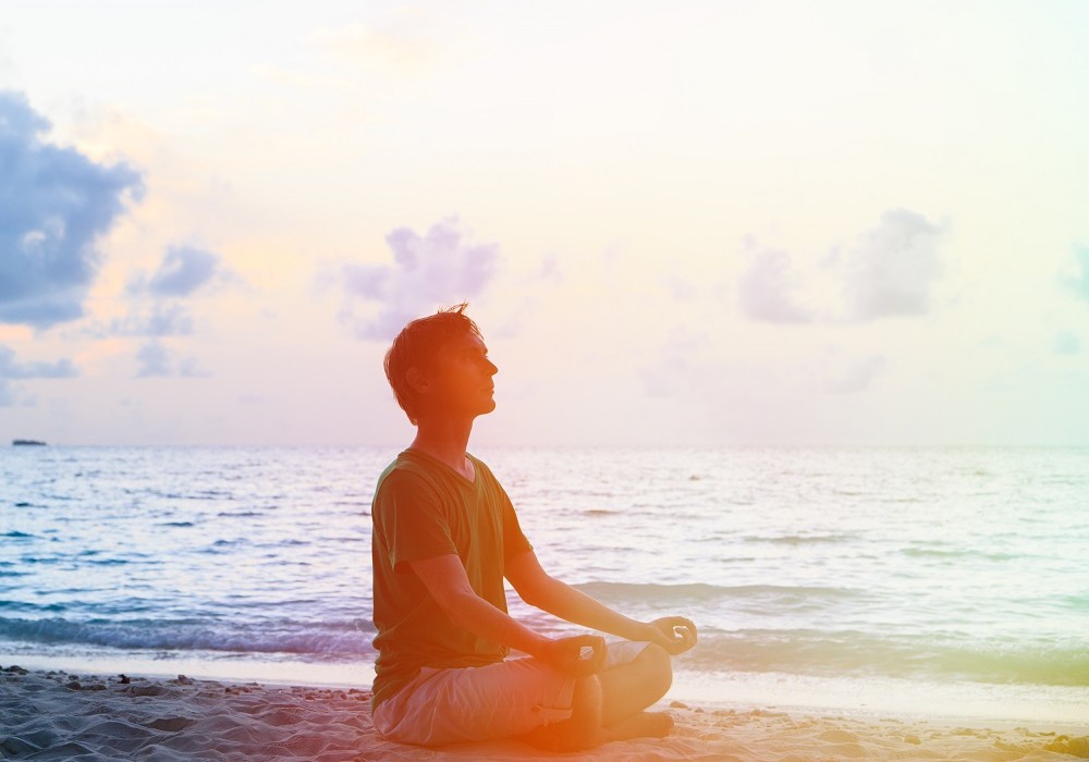 Silhouette of young man meditating at sunset beach