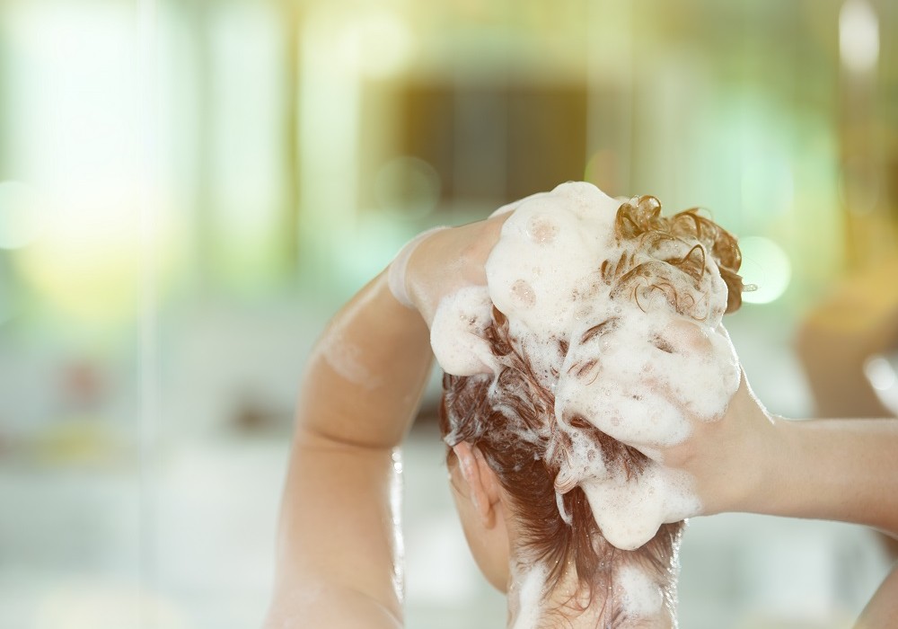 rear view of woman washing her red hair, hands in hair.