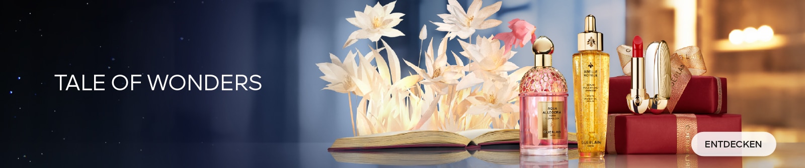 Guerlain Tale of Wonders: Ein rosa Guerlain Aqua Allegoria Parfümflakon, eine goldene Guerlain Abeille Royale Serumflasche und ein roter Guerlain Lippenstift in einem goldenen Etui auf einem sanften floralen Hintergrund mit Geschenkboxen.