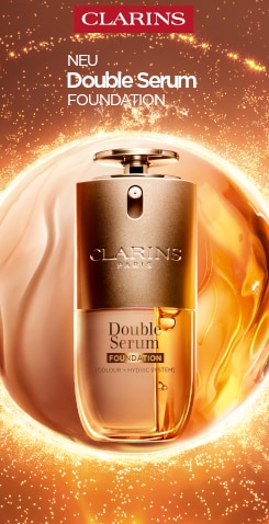 Clarins Double Serum Foundation in goldenem Flakon vor wirbelndem, leuchtendem Hintergrund – neue Foundation mit Pflege‑Effekt.
