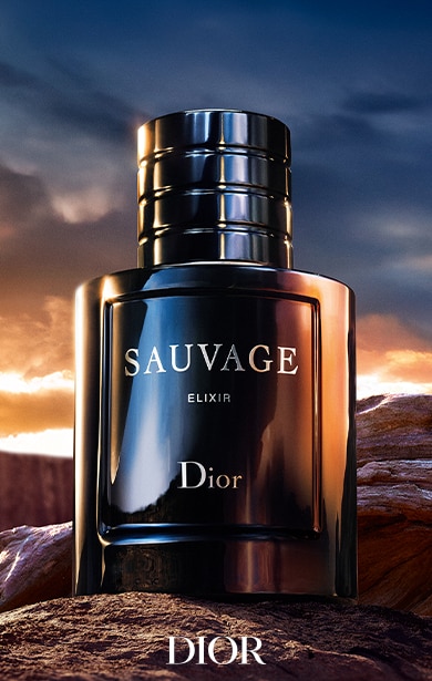 Eine Flasche Dior Sauvage Elixir Parfüm liegt auf einer felsigen Oberfläche, vor einem dramatischen Sonnenuntergangshimmel.