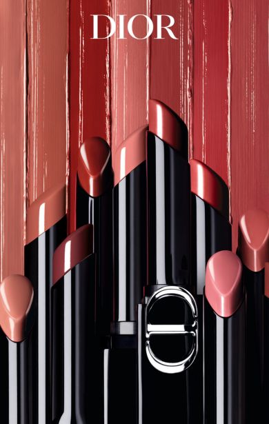 Eine Sammlung von Dior-Lippenstiften in verschiedenen Rosa-, Rot- und Nude-Tönen, gestaffelt angeordnet mit geöffneten Kappen, sodass die Farben sichtbar sind. Im Hintergrund sind vertikale Farbstreifen der gleichen Lippenstifttöne zu sehen.
