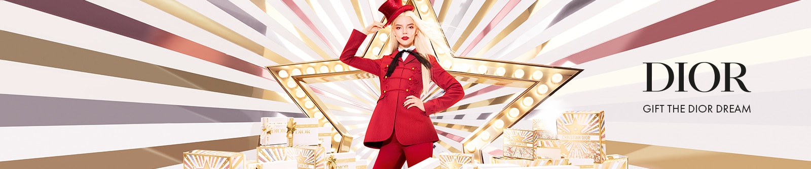 Dior: Gift the Dior Dream - Anya Taylor-Joy in einem roten Outfit mit passendem Hut steht vor einem großen beleuchteten Stern, umgeben von Geschenkboxen mit Dior-Logo.