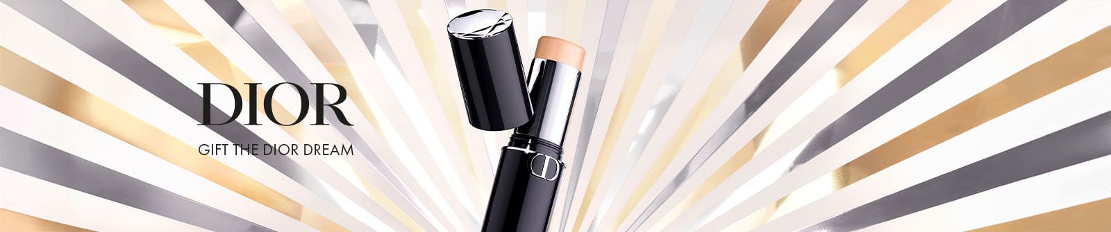 Dior: Gift the Dior Dream - Dior Foundation-Stick mit abgenommener Kappe, präsentiert in einem eleganten schwarzen und silbernen Design mit &apos;CD&apos;-Logo, vor einem strahlenden Hintergrund aus goldenen und silbernen Strahlen.
