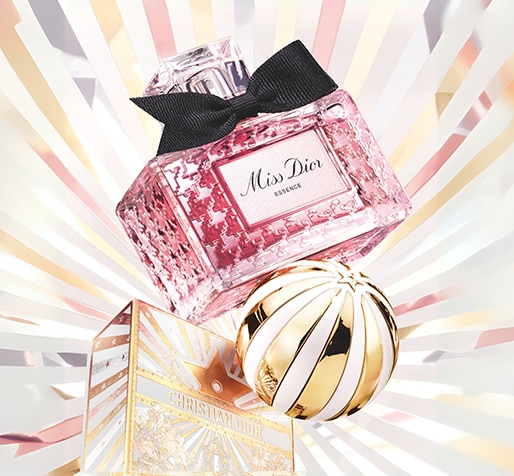 Dior_Xmas_MRD_Matrix_Banner_Large_514x476px_01_MissDior.png Rosa Miss Dior Essence-Parfümflakon mit schwarzer Schleife oben, platziert über einer gold-weiß gestreiften Kugel und einer dekorativen Box mit der Aufschrift ‚Christian Dior‘ vor einem Hintergrund aus goldenen, silbernen und bronzenen Sternstrahlen.